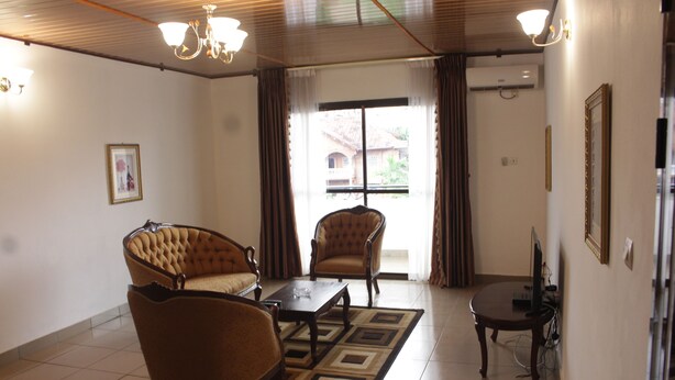 A living room with a sofa, armchairs, a coffee table, and a TV. - Gold Court Appartements Meublés (Yaoundé)