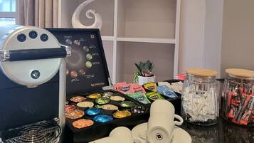 A coffee station with a Nespresso machine, a selection of coffee pods, and a small potted plant.