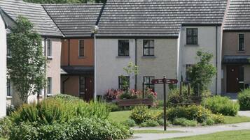 A row of townhouses with a well-maintained garden in front, a signpost indicating house numbers, and a clear sky above.