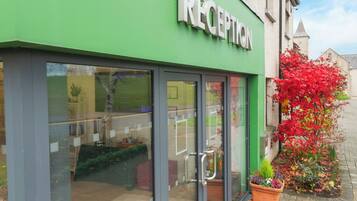 A reception area with a green facade, large glass windows, and potted plants outside.
