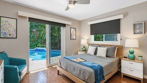 A bedroom with a bed, a nightstand, a desk, a chair, a ceiling fan, and a sliding glass door leading to a pool. - Modern Tropical Oasis, Private Heated Pool, Near Beaches! (Wilton Manors)
