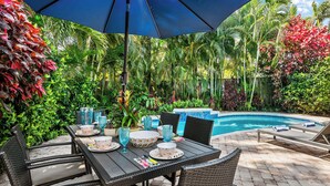 A poolside area with a table set for dining, surrounded by lush tropical plants and a clear blue sky. - Modern Tropical Oasis, Private Heated Pool, Near Beaches! (Wilton Manors)