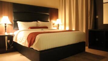 Habitación de hotel con una cama grande, dos mesitas de noche con lámparas, un cabecero oscuro y vistas a un paisaje urbano por la ventana.
