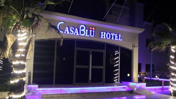 Exterior del hotel CasaBlü con señalización iluminada, grandes puertas de vidrio y un área de entrada bien iluminada.