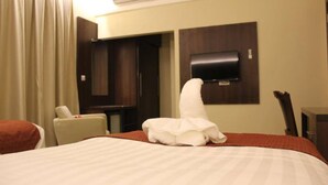 Habitación de hotel con una cama grande, una silla, un escritorio, un televisor de pantalla plana montado en la pared y una ventana con cortinas.