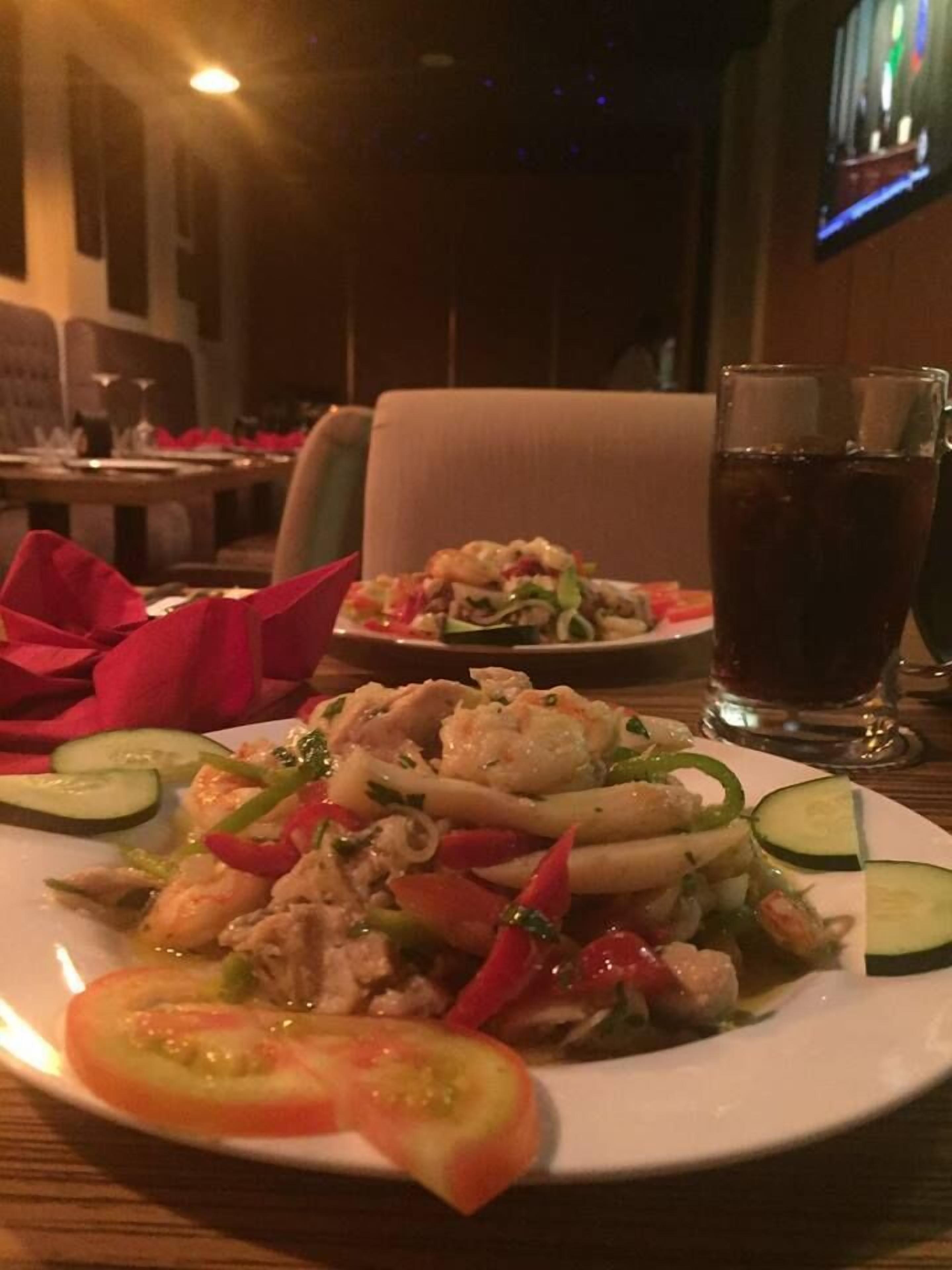 A dining table with a plate of food, a glass of dark beverage, and a red napkin.