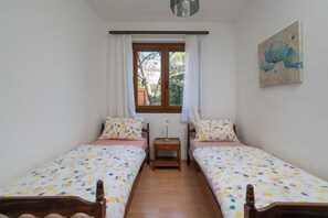 Une chambre avec deux lits simples, une fenêtre avec des rideaux, une table de chevet et un tableau au mur.