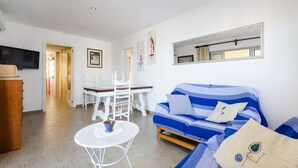 Un salon avec un canapé à rayures bleues, une table à manger blanche et un téléviseur fixé au mur.