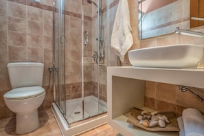 A modern bathroom with a glass-enclosed shower, a white toilet, and a sink with a wooden tray.