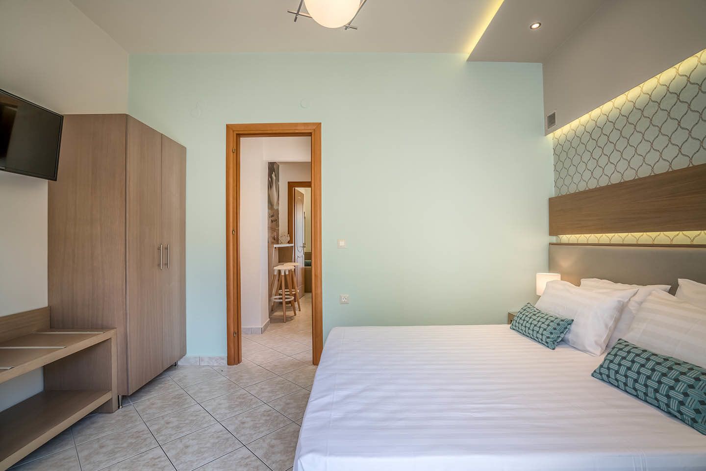 A modern bedroom with a large bed, a TV, wooden wardrobe, and a walk-in closet.