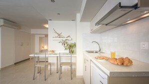 A modern kitchen with white cabinetry, a stainless steel sink, and a countertop with croissants and a glass of orange juice. - Alba Boutique Apartments (Zakynthos)