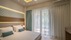A hotel room with a large bed, a bedside table with a lamp, a ceiling light, an air conditioning unit, and a view of the outdoors through sheer curtains. - Alba Boutique Apartments (Zakynthos)