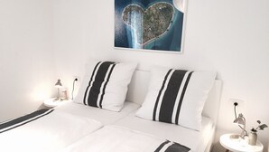 Une chambre d’hôtel bien aménagée, avec un grand lit, deux tables de chevet et une œuvre d’art représentant un cœur, accrochée au mur.