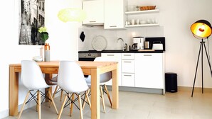 Une cuisine moderne avec des meubles blancs, une table à manger en bois avec quatre chaises, une poubelle noire et un lampadaire.