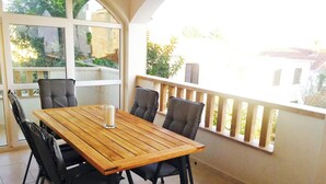 Une table à manger en bois, accompagnée de quatre chaises, d’une bougie blanche et d’un balcon doté d’une balustrade.