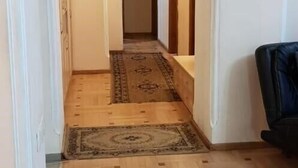 A hallway with wooden flooring, a patterned rug, and a black leather chair. - Apartament on Shartava str. (Tbilisi)