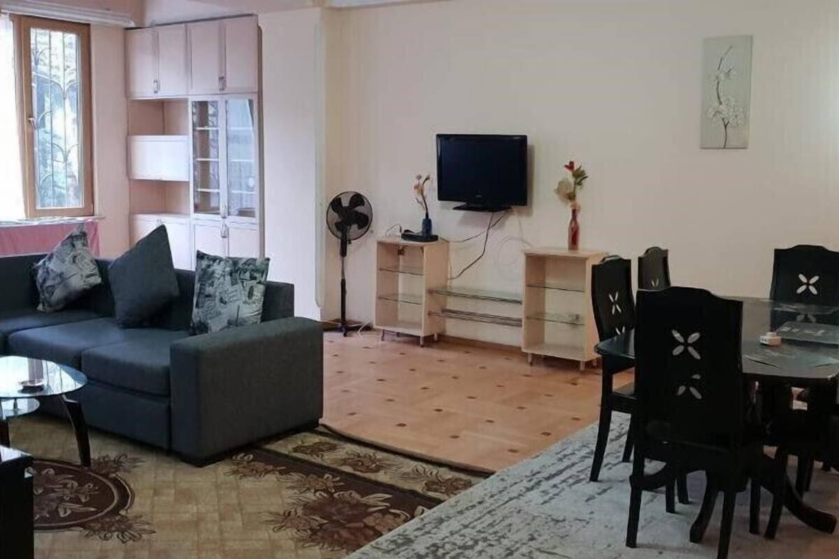 Una sala de estar con un sofá, una mesa de comedor con sillas, un televisor y un ventilador.