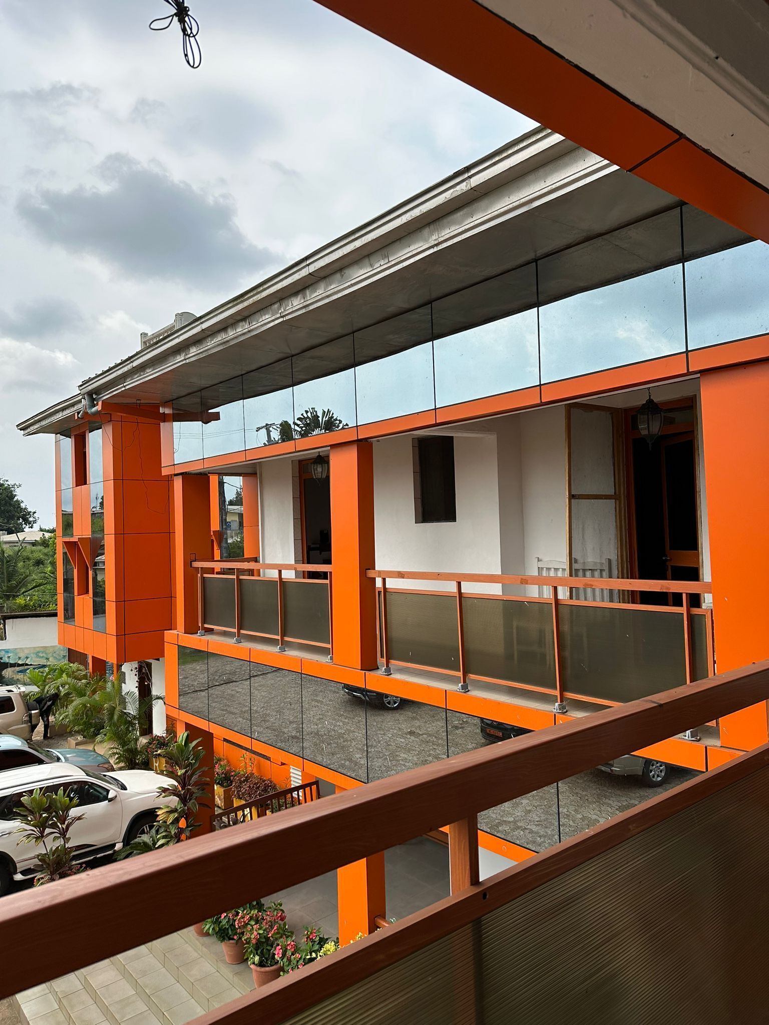 A multi-story building with orange and white exterior walls, large windows, and a balcony with a wooden railing.