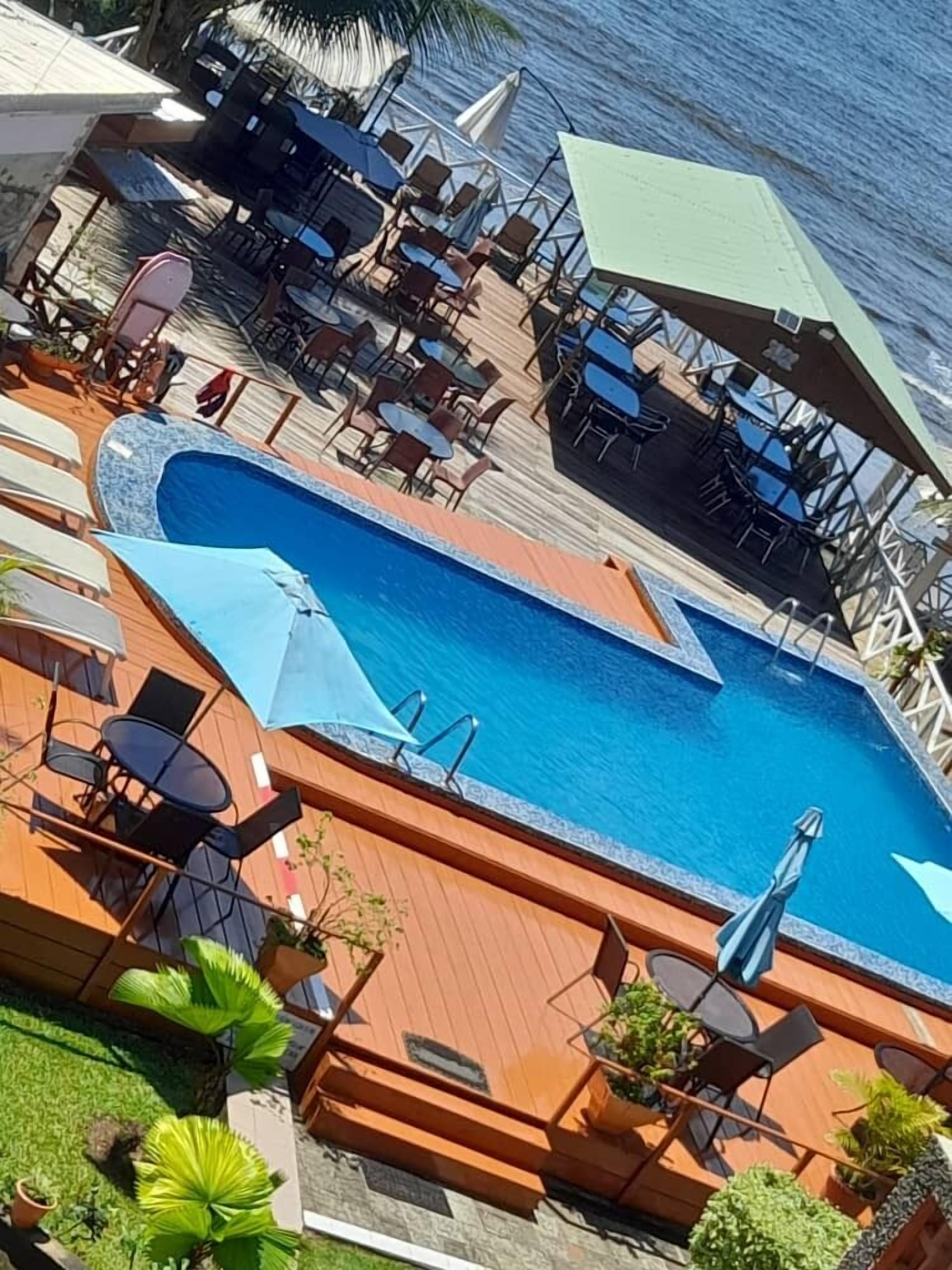 Zona junto a la piscina con sillones, sombrillas y vista al océano.