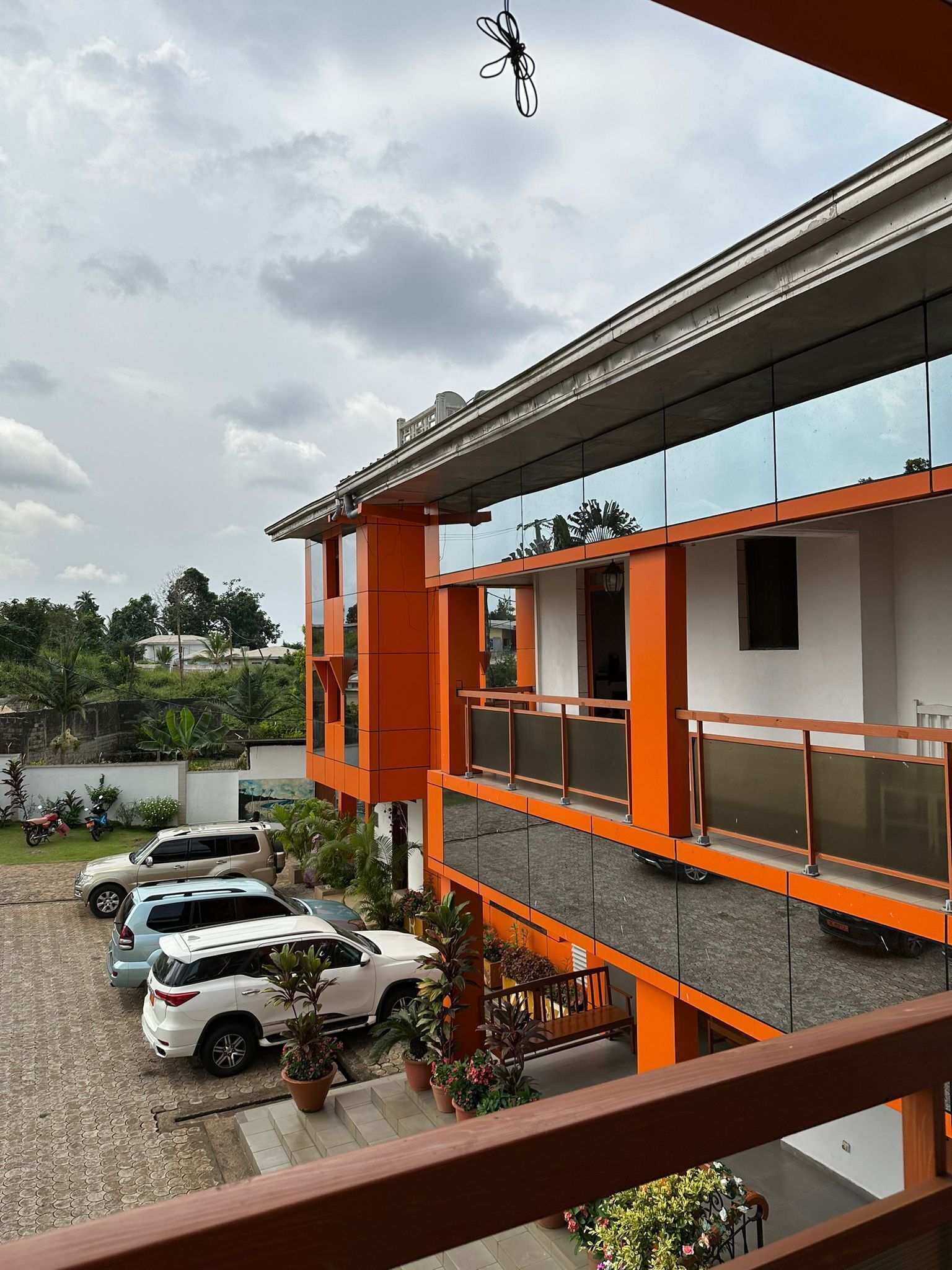 A multi-story building with orange and white exterior walls, a covered parking area with several cars, and a view of the sky through the windows.