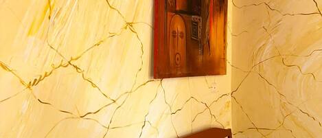 Un banco de madera apoyado en una pared con superficie texturizada y agrietada, y un cuadro colgado encima.