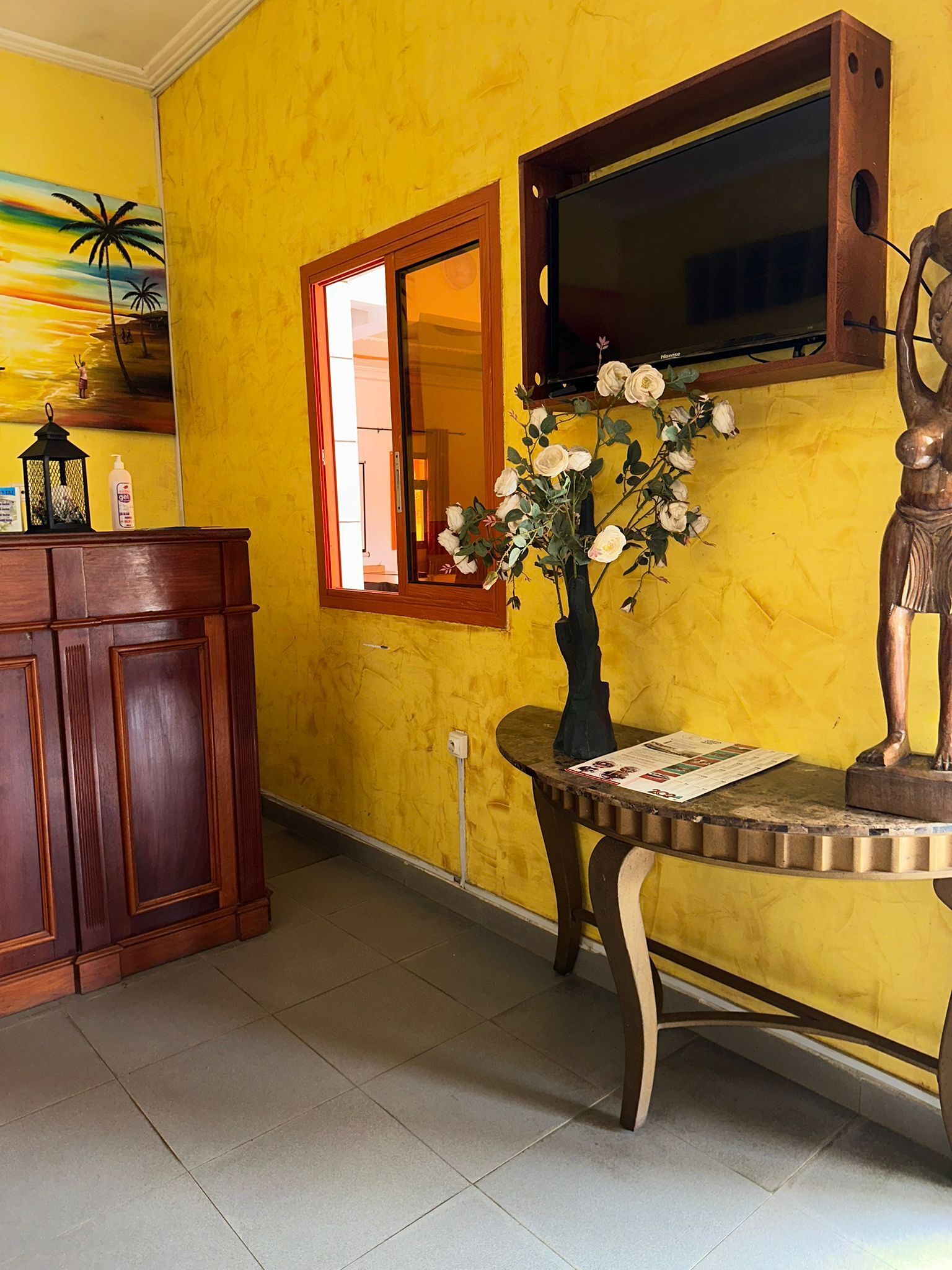 A room with a yellow wall, a wooden cabinet, a small table with a vase of flowers, and a mounted television.