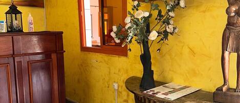 A room with a yellow wall, a wooden cabinet, a small table with a vase of flowers, and a mounted television.