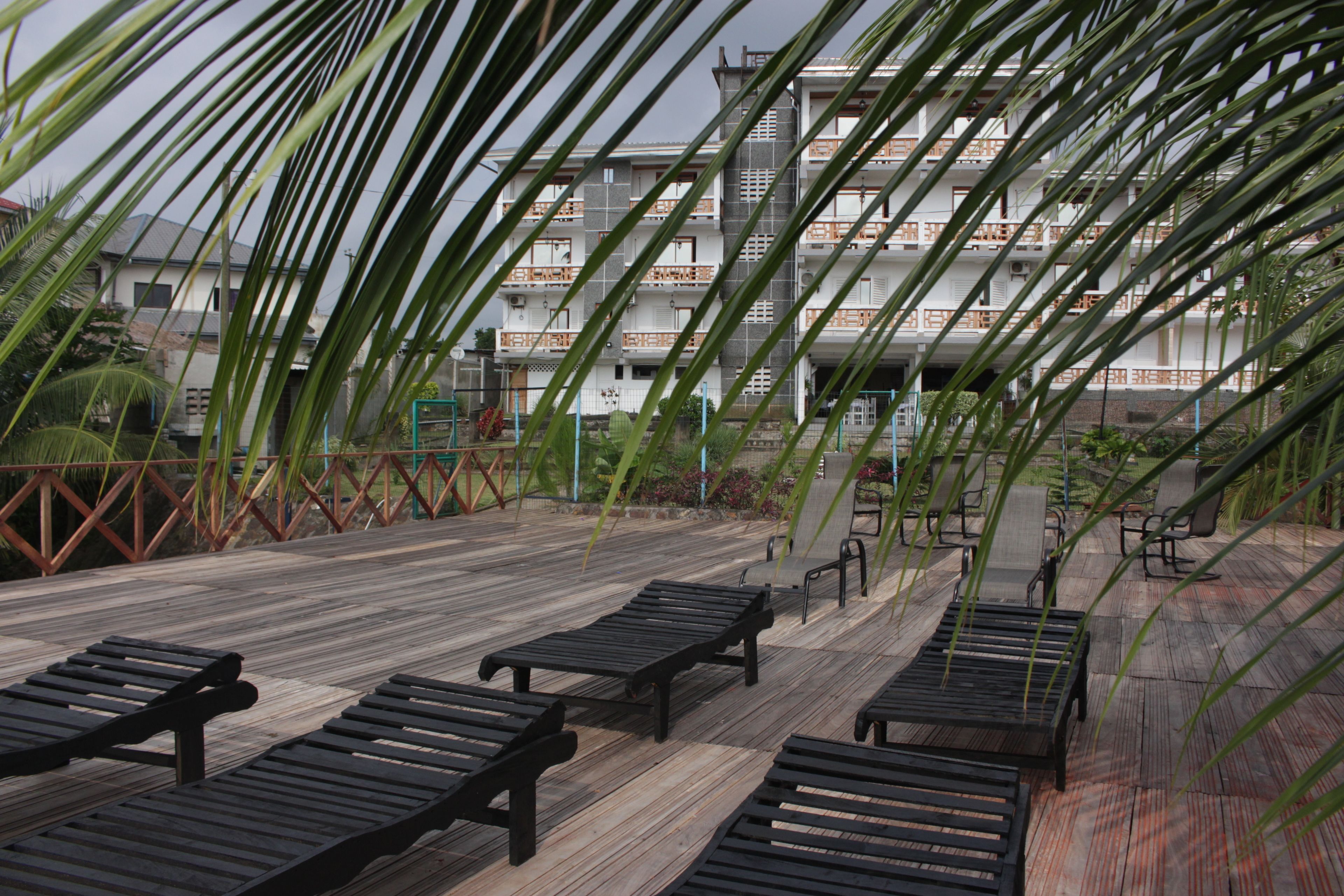 A wooden deck with lounge chairs, a metal fence, and a building with multiple balconies in the background.