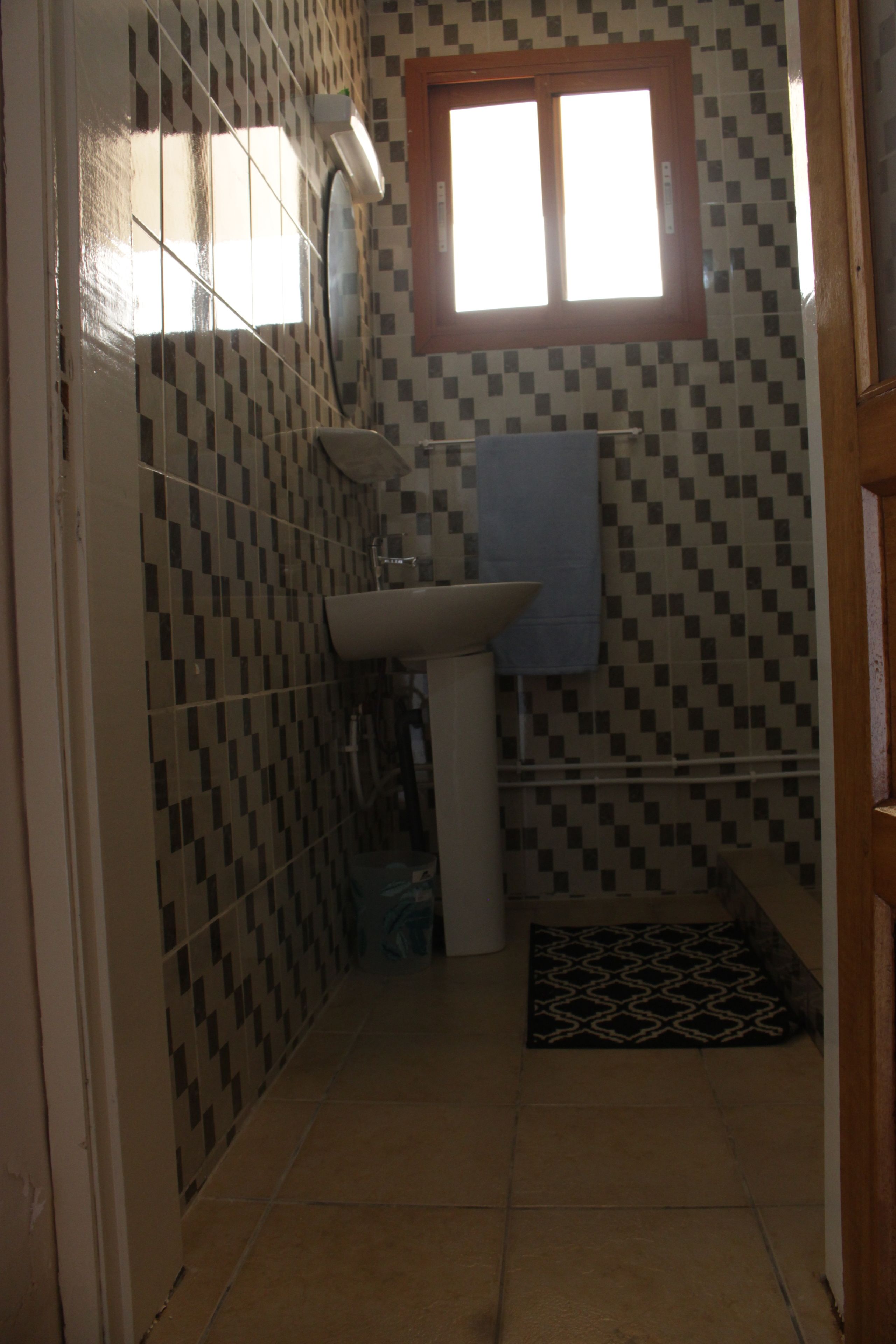 A small bathroom with a tiled floor, a sink, a window, and a door.