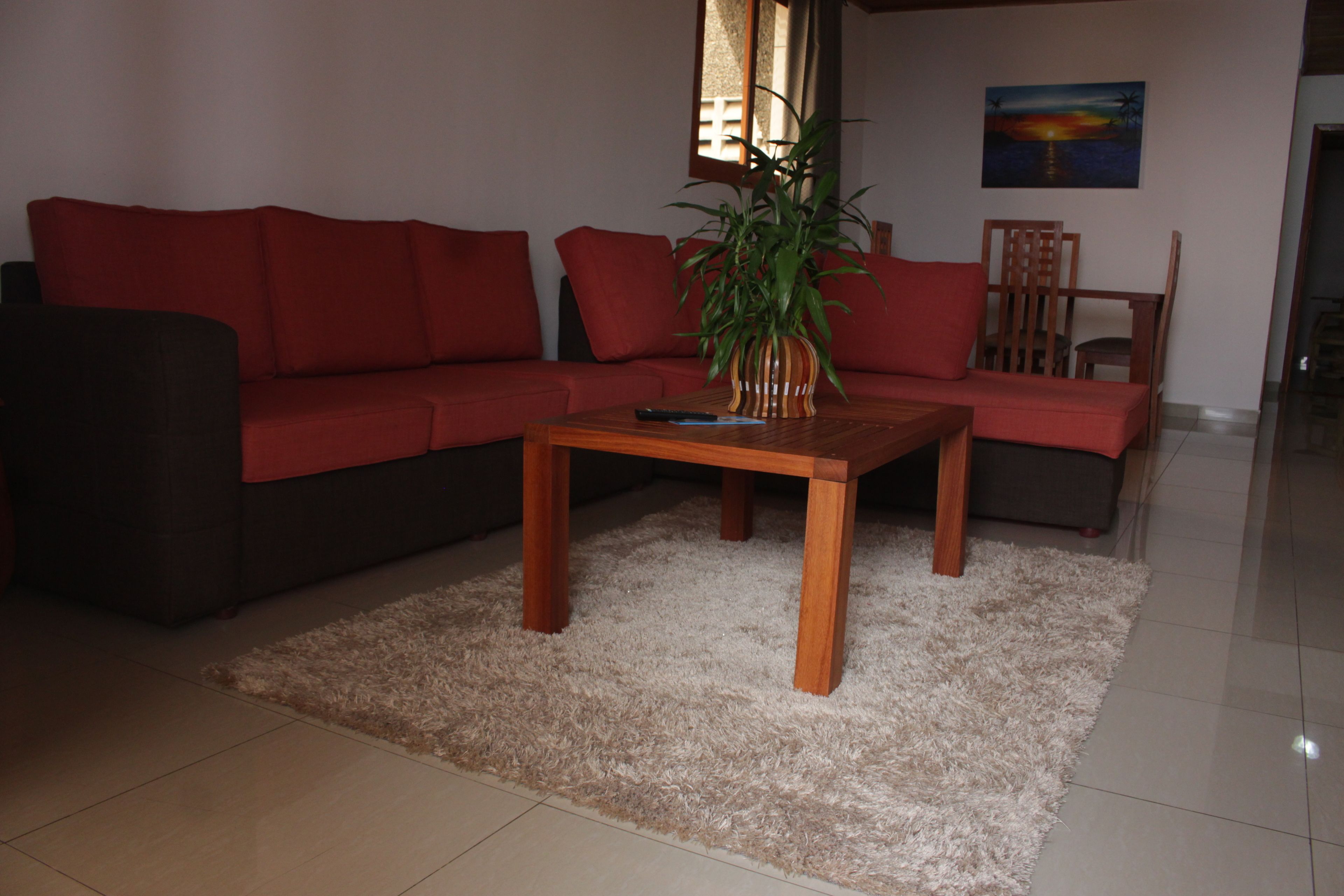 Una sala de estar con un sofá rojo, una mesa de centro de madera y una planta en maceta.