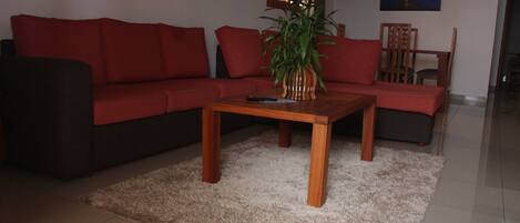 Una sala de estar con un sofá rojo, una mesa de centro de madera y una planta en maceta.