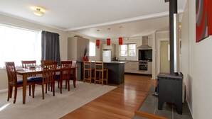 Una cocina moderna con una isla central, un comedor con sillas de madera y una estufa a leña.