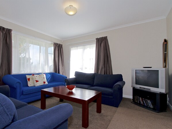 A living room with two blue sofas, a wooden coffee table, a television on a stand, and a bookshelf.