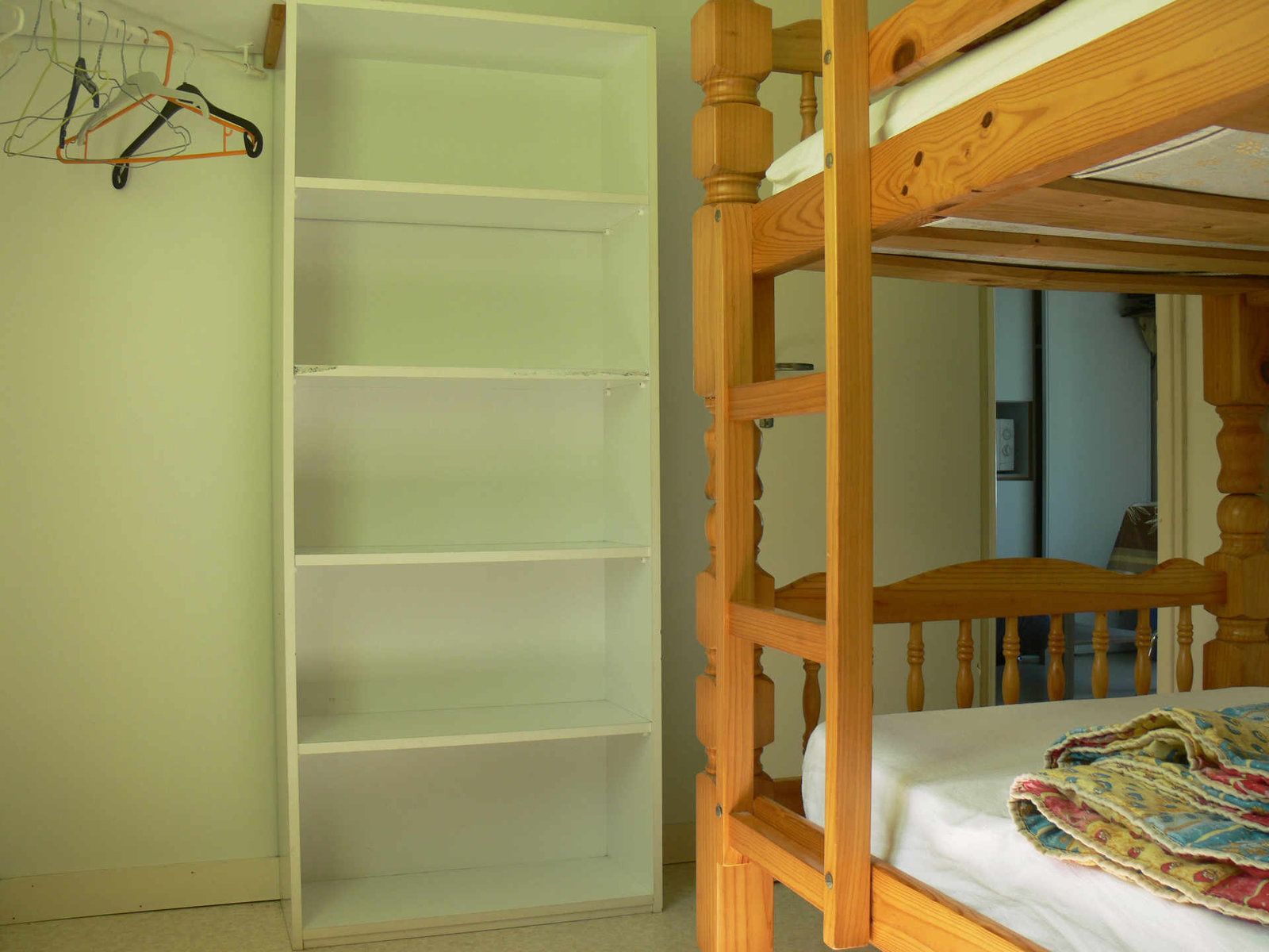 A bunk bed with a wooden frame and a lower shelf, a white wardrobe with multiple compartments, and a clothes rack with hangers.