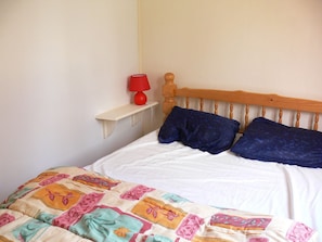 A bed with a wooden headboard, a red lamp on a small shelf, and a colorful quilt.