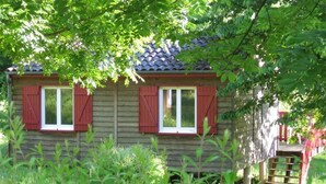 A rustic wooden house with red shutters, surrounded by lush greenery. - Camping le Repaire - Les Chalets (Thiviers)