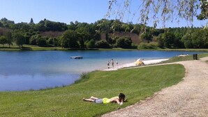 A lakeside scene with a grassy area, a dock, and a path leading to a sandy beach. - Camping le Repaire - Les Chalets (Thiviers)
