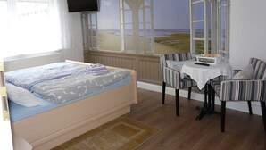 A bedroom with a bed, a TV, a window with a beach view, a small table, and a chair. - Pension Zur Kirchsee (Insel Poel)
