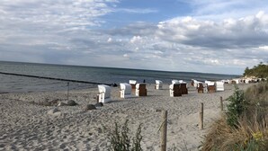 A beach with rows of white beach chairs and wooden structures, likely for sunbathing or relaxation, under a partly cloudy sky. - Pension Zur Kirchsee (Insel Poel)