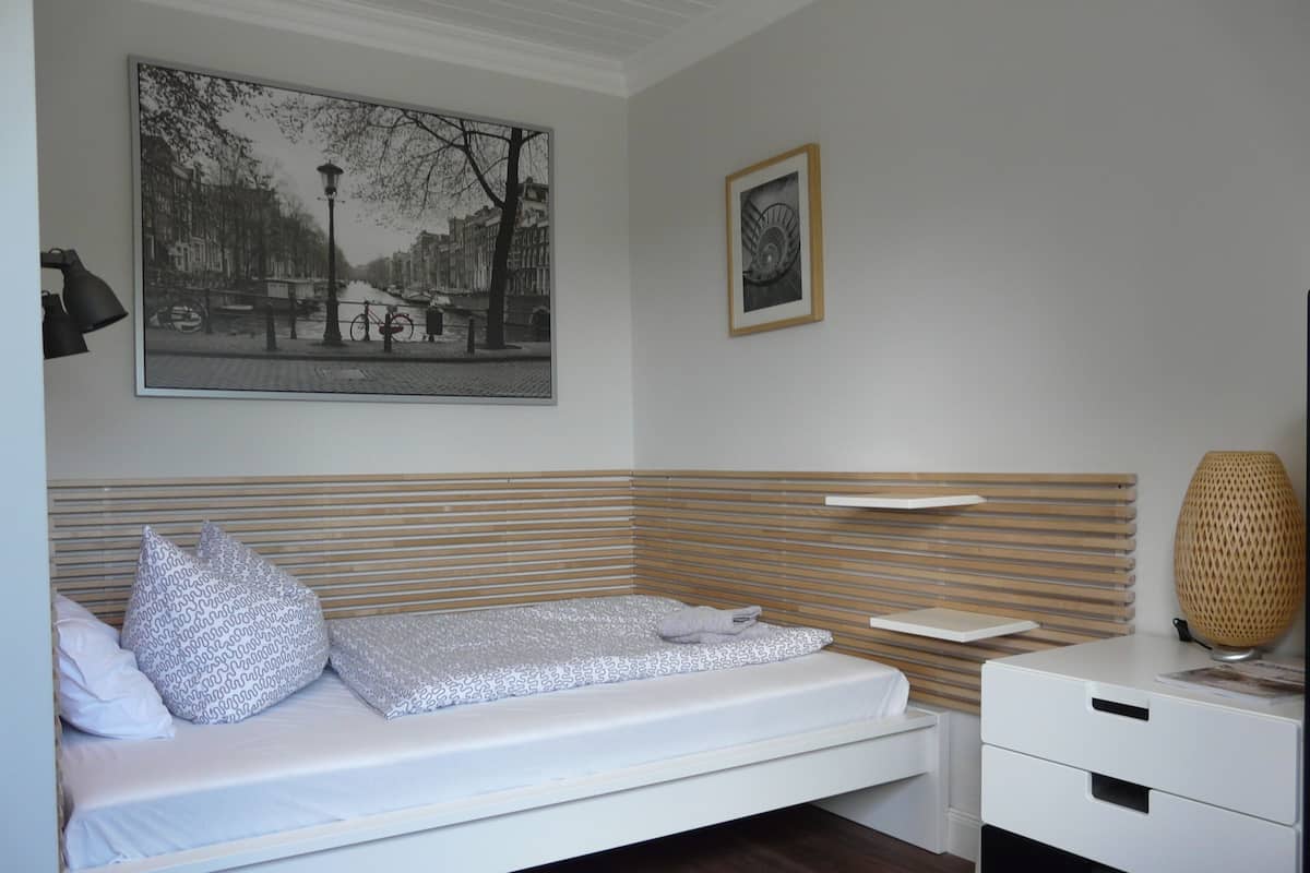 A neatly arranged bedroom with a single bed, a bedside table, a lamp, and a framed picture on the wall.