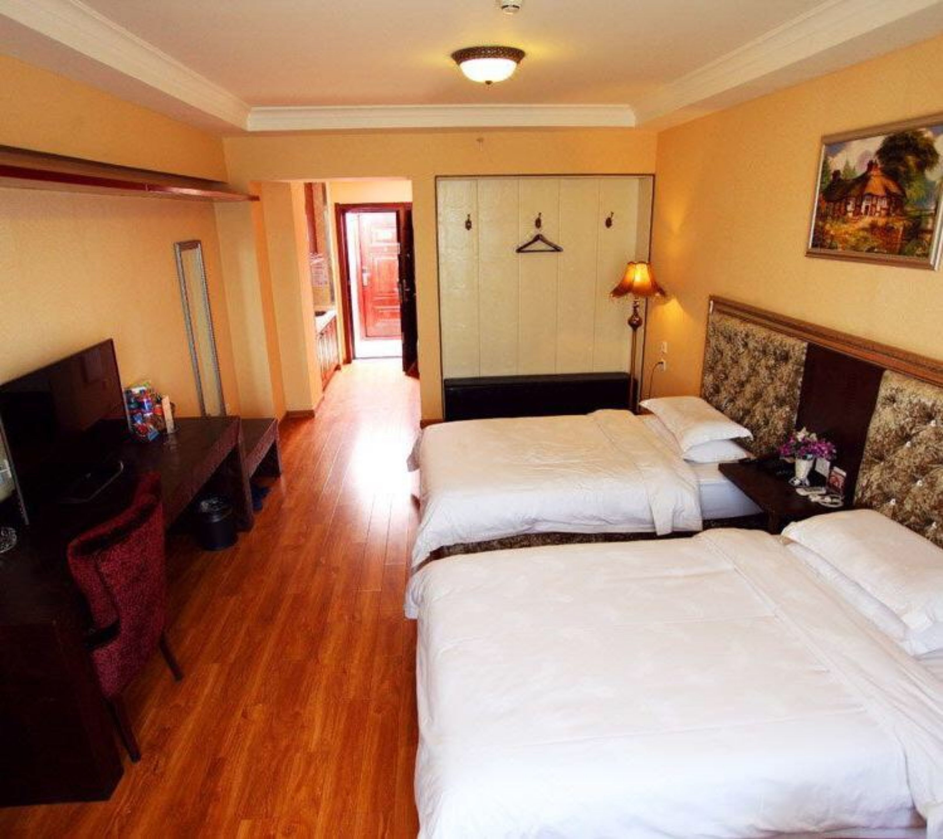 A hotel room with two beds, a desk, a chair, a TV, and a painting on the wall.