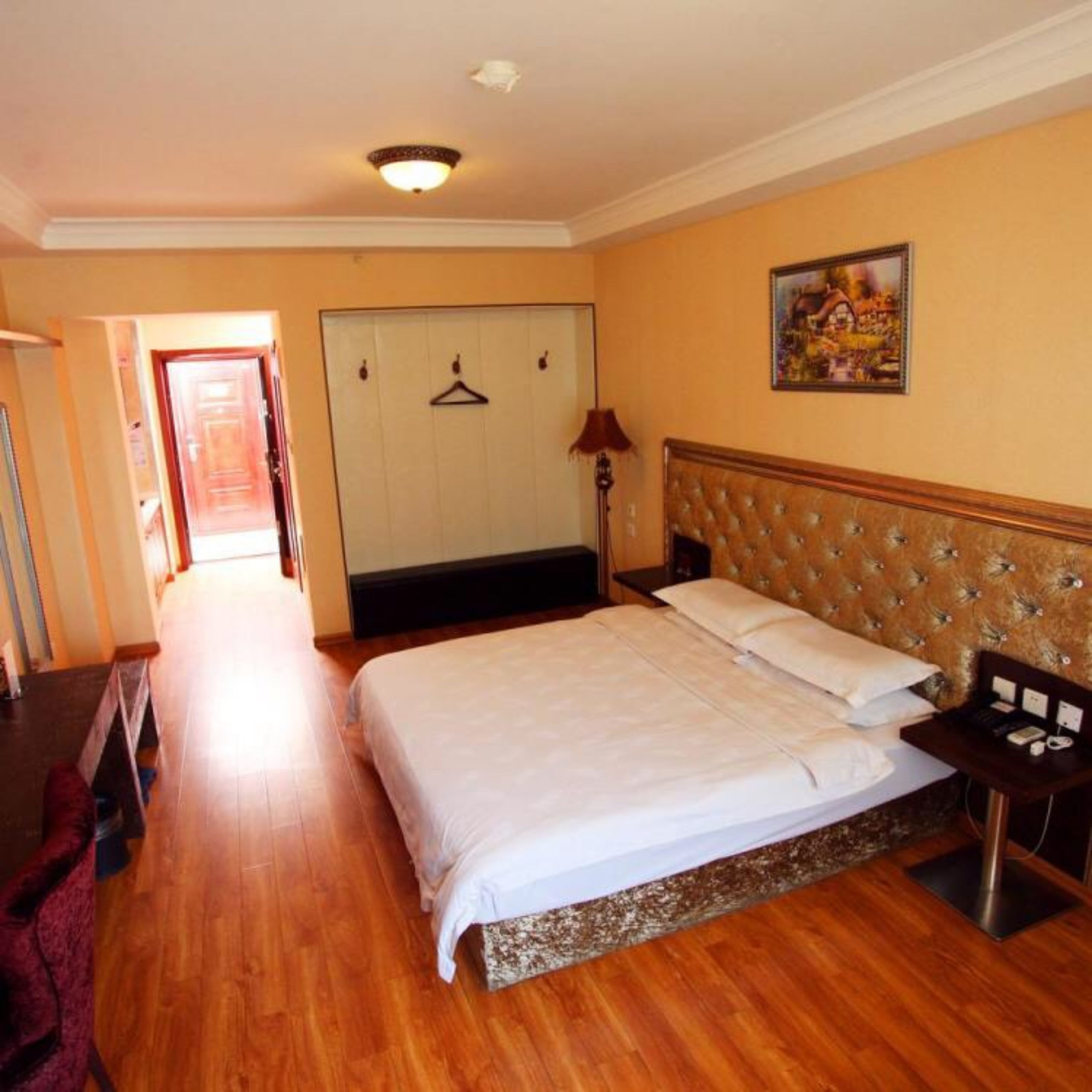 A hotel room with a large bed, a wooden floor, a wardrobe, and a painting on the wall.