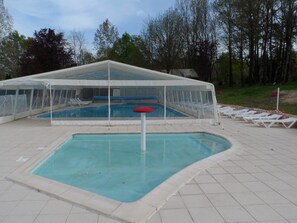 Une piscine couverte avec des chaises longues et un auvent.