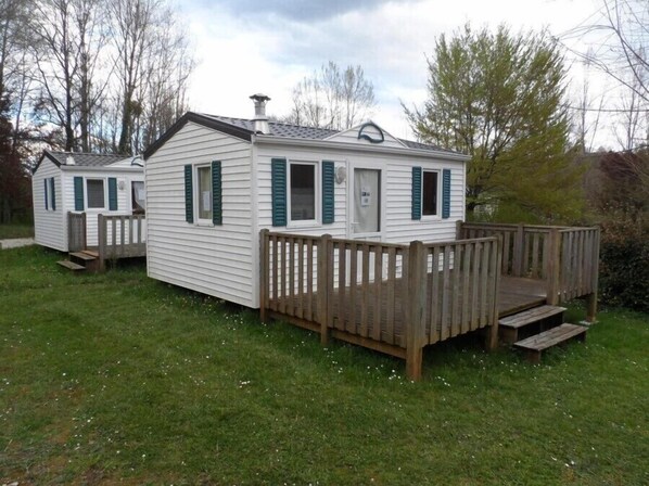 Une petite maison mobile d’un seul étage, dotée d’une terrasse en bois et d’une cheminée.