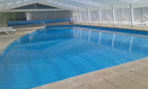 An indoor swimming pool with clear blue water, a diving board, and a covered seating area. - CAMPING LE REPAIRE - MOBILHOME 20m2 (Thiviers)