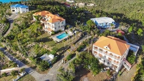An aerial view of a coastal resort with multiple buildings, a swimming pool, and a view of the sea and mountains. - Coconut Tree Villa (East End)