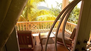 A balcony with wooden chairs and a view of palm trees and mountains. - Coconut Tree Villa (East End)