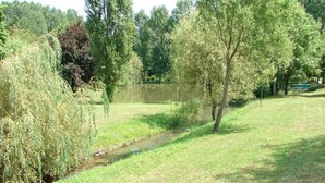 A serene park with a small stream, lush greenery, and a distant boat on the water.
