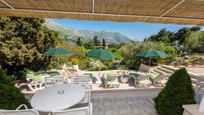Une terrasse extérieure avec des chaises et des tables blanches, des parasols verts et une vue sur les montagnes.