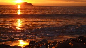 A sunset over the ocean with a rocky shoreline.